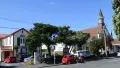 Colour photograph of buildings and a tree, red car parked on the street