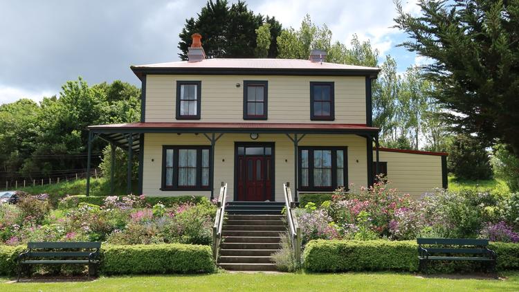 Yellow house in a garden of flowers and a green lawn