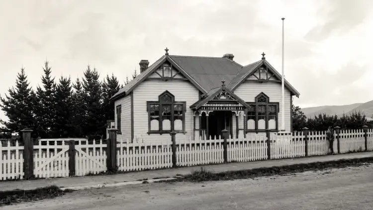 Sepia photograph of a house with dark roof and white picket fence, flag pole