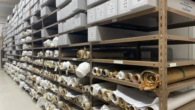 Photo of archival shelfing with rolled maps and grey containers and boxes.