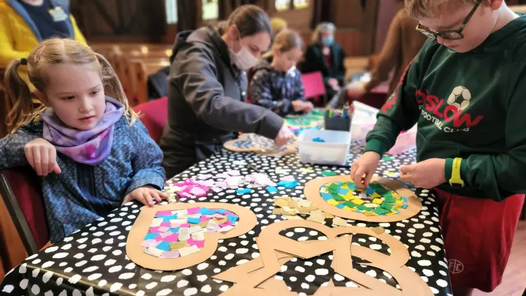 Colour photograph of children pasting paper crafts on a table with a black and white pattern.