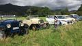 Photo of a mixture of vintage vehicles and one modern vehicle in a field. 