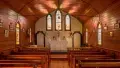 Inside of a wooden church with pews and stained glass windows