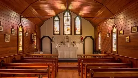 Inside of a wooden church with pews and stained glass windows